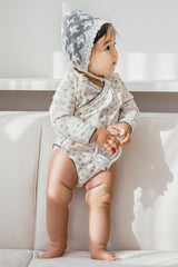 Toddler standing in the Avauma Cream Bodysuit (Spring Forest) – emphasizing the flexible long-sleeve design, soft texture, and adorable blue floral accents for active babies. Toddler standing in the Avauma Cream Bodysuit (Spring Forest) – emphasizing the flexible long-sleeve design, soft texture, and adorable blue floral accents for active babies.