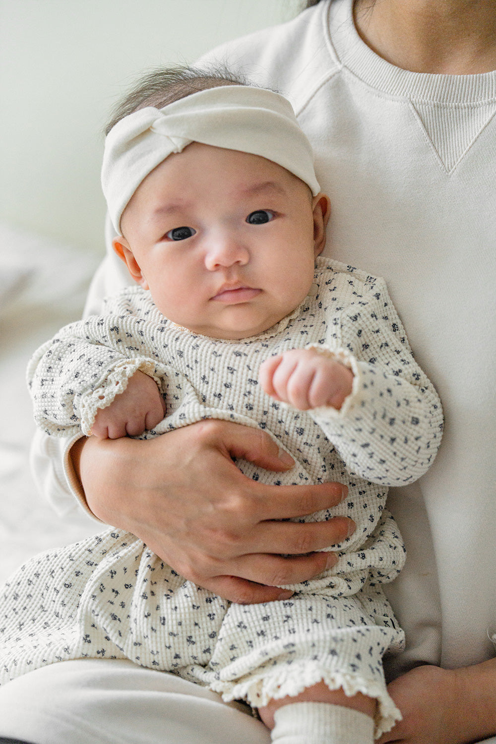 Baby in the Olive Rose bodysuit held by a caregiver – combining a natural ivory tone with a floral pattern for a warm, cozy impression. Baby in the Olive Rose bodysuit held by a caregiver – combining a natural ivory tone with a floral pattern for a warm, cozy impression.