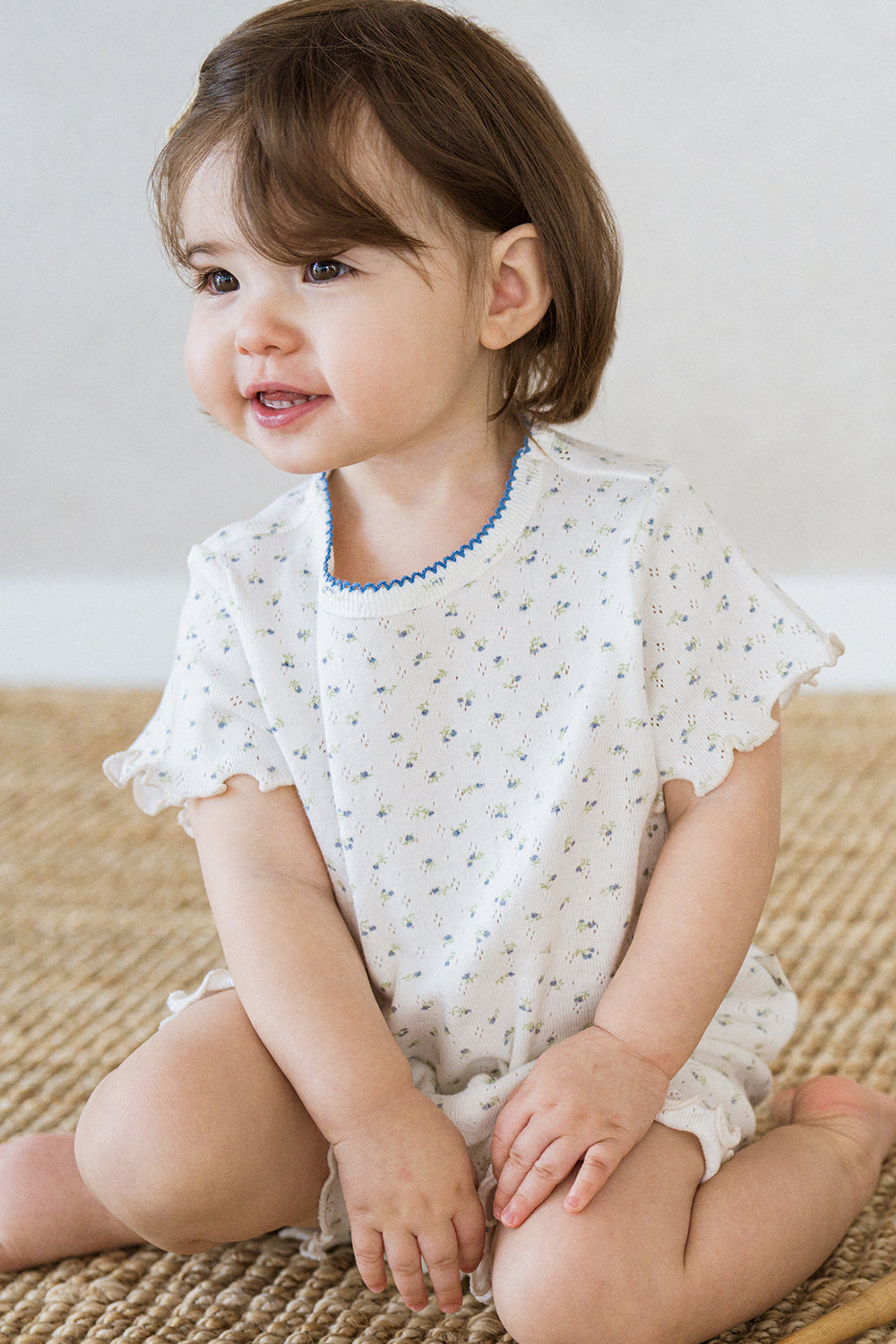 Toddler girl smiling in Avauma Mellow Days Vanilla Herb summer outfit, with blue trim neckline and ruffled sleeves. Soft and breathable baby clothes. Toddler girl smiling in Avauma Mellow Days Vanilla Herb summer outfit, with blue trim neckline and ruffled sleeves. Soft and breathable baby clothes.