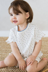 Toddler girl smiling in Avauma Mellow Days Vanilla Herb summer outfit, with blue trim neckline and ruffled sleeves. Soft and breathable baby clothes. Toddler girl smiling in Avauma Mellow Days Vanilla Herb summer outfit, with blue trim neckline and ruffled sleeves. Soft and breathable baby clothes.