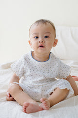 Baby boy in Mellow Days Vanilla Herb baby set by Avauma, sitting on a bed. Adorable summer pajamas in white with tiny green floral design. Baby boy in Mellow Days Vanilla Herb baby set by Avauma, sitting on a bed. Adorable summer pajamas in white with tiny green floral design.