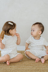 Two toddlers in matching Avauma Mellow Days Vanilla Herb summer sets, sitting together on a mat. Cozy, soft baby loungewear with floral print. Two toddlers in matching Avauma Mellow Days Vanilla Herb summer sets, sitting together on a mat. Cozy, soft baby loungewear with floral print.