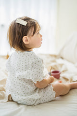 Toddler girl sitting on bed in Avauma Mellow Days Set Vanilla Herb, back view. Sweet ruffled edges and light green floral pattern for summer. Toddler girl sitting on bed in Avauma Mellow Days Set Vanilla Herb, back view. Sweet ruffled edges and light green floral pattern for summer.