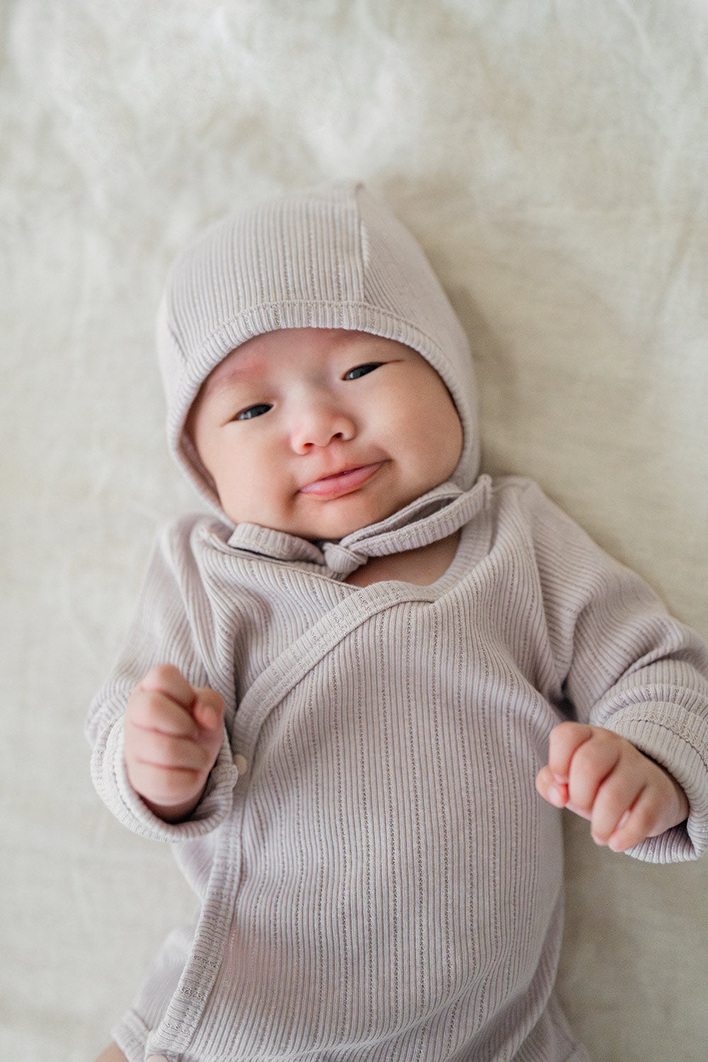 Close-up of a smiling baby in the Avauma Selina Babysuit (lavender haze), featuring gentle ribbed texture and secure snap buttons for newborns and young infants.
 Close-up of a smiling baby in the Avauma Selina Babysuit (lavender haze), featuring gentle ribbed texture and secure snap buttons for newborns and young infants.