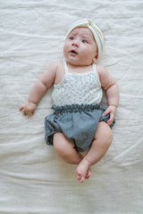 Baby wearing Avauma Lily Sleeveless Bodysuit Cream Blue. Infant in a white floral print bodysuit, dark blue checkered bloomers, and a white headband.
Baby wearing Avauma Lily Sleeveless Bodysuit Cream Blue. Infant in a white floral print bodysuit, dark blue checkered bloomers, and a white headband.