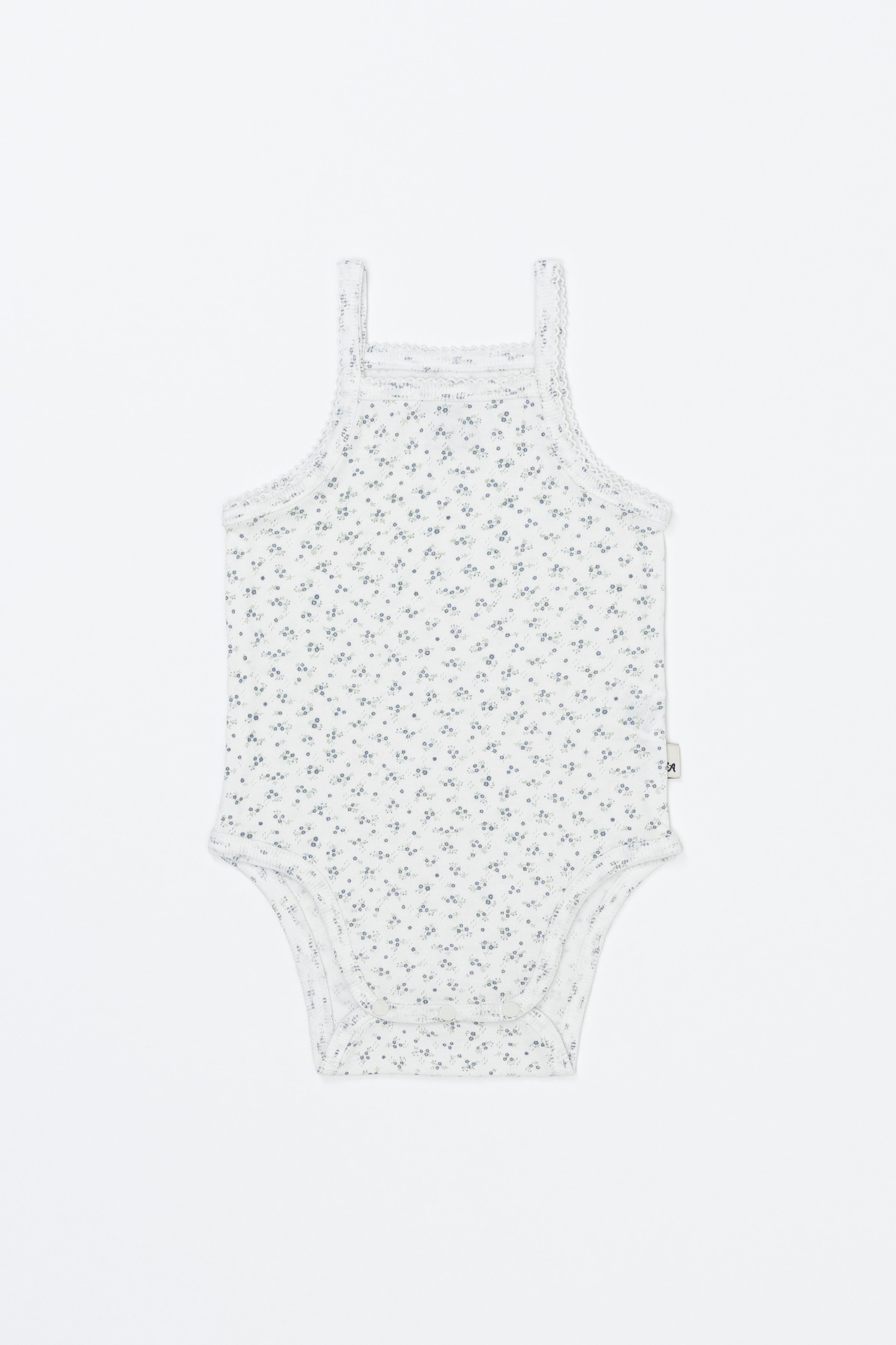 Avauma Lily Sleeveless Bodysuit Cream Blue product shot. Lay-flat of white sleeveless baby romper with small blue floral print on a white background. Avauma Lily Sleeveless Bodysuit Cream Blue product shot. Lay-flat of white sleeveless baby romper with small blue floral print on a white background.