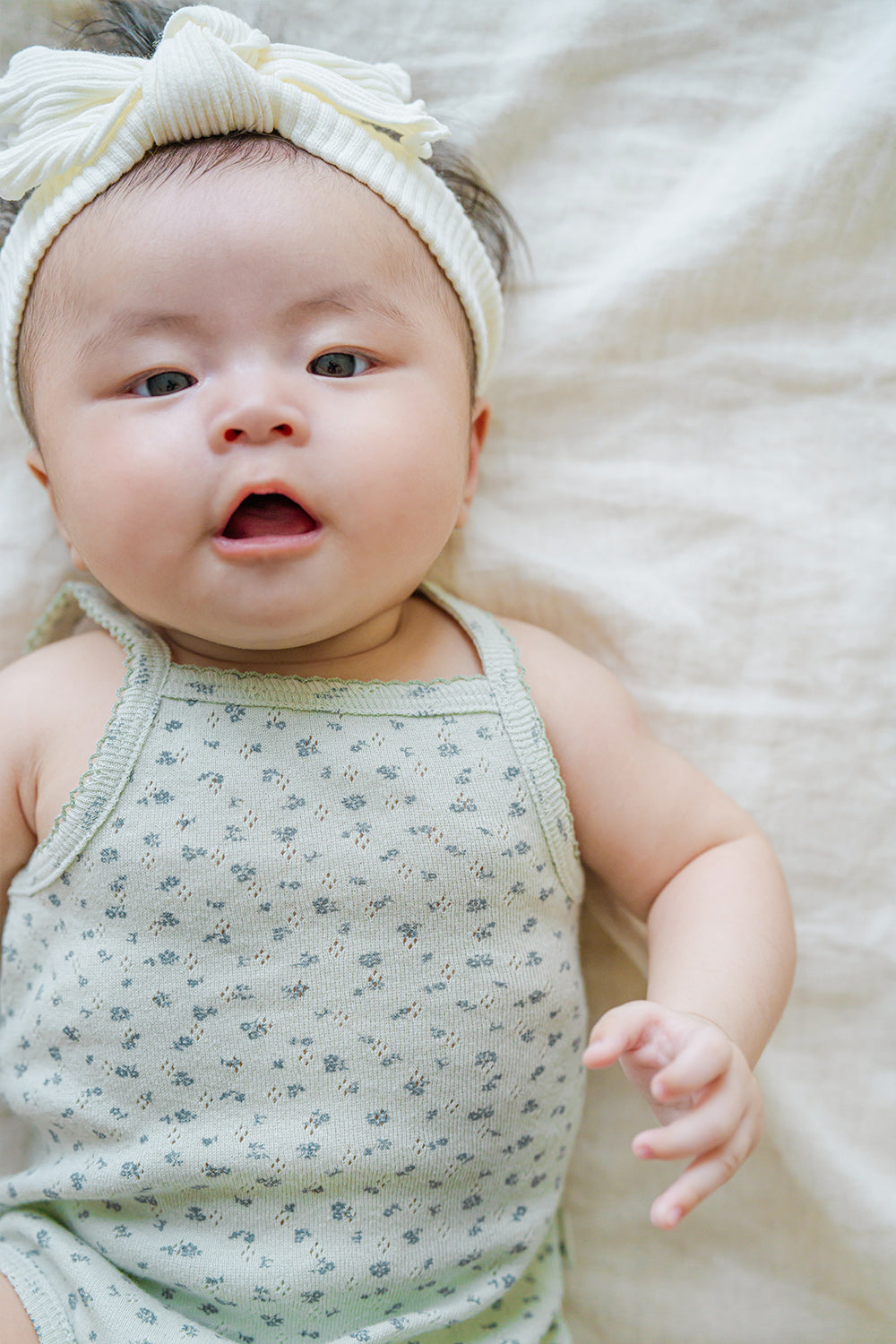 Happy baby face in Avauma Lily Sleeveless Bodysuit Sage Flower. Infant looking at camera, wearing a sage green floral romper and white twisted headband.
Happy baby face in Avauma Lily Sleeveless Bodysuit Sage Flower. Infant looking at camera, wearing a sage green floral romper and white twisted headband.