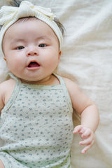 Happy baby face in Avauma Lily Sleeveless Bodysuit Sage Flower. Infant looking at camera, wearing a sage green floral romper and white twisted headband.
Happy baby face in Avauma Lily Sleeveless Bodysuit Sage Flower. Infant looking at camera, wearing a sage green floral romper and white twisted headband.