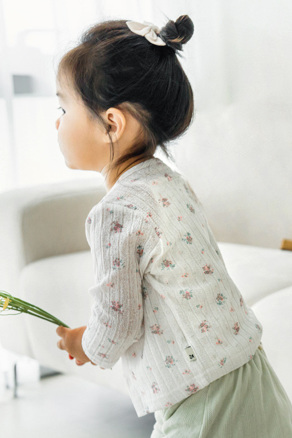 Toddler girl in avauma Rosy Cream Flower Cardigan sitting sideways, holding greenery, wearing light green shorts.
Toddler girl in avauma Rosy Cream Flower Cardigan sitting sideways, holding greenery, wearing light green shorts.