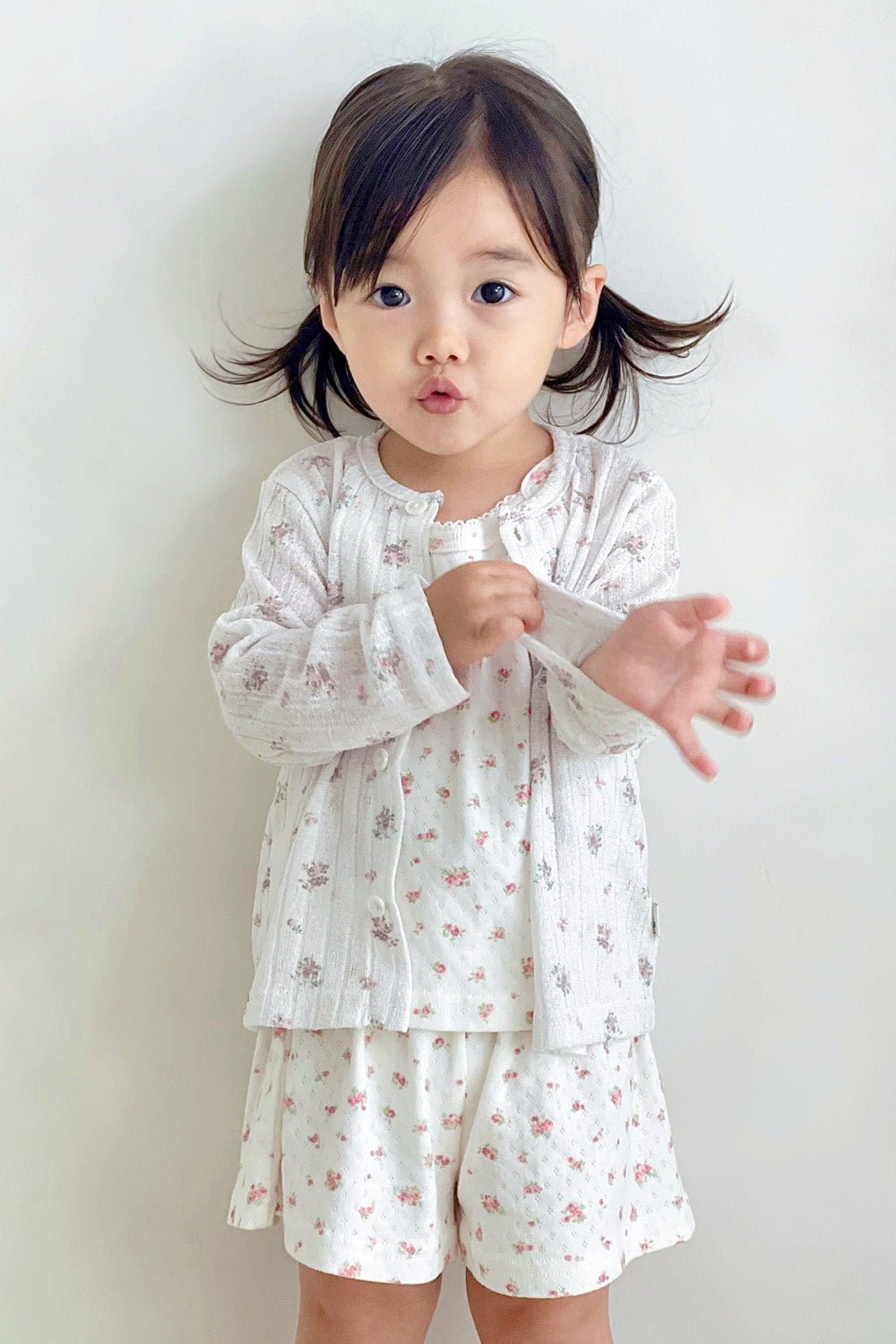 Toddler girl posing in avauma Rosy Cream Flower Cardigan and matching shorts set, smiling indoors. Toddler girl posing in avauma Rosy Cream Flower Cardigan and matching shorts set, smiling indoors.