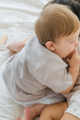 Back view of a baby model wearing the ivory Lucent Short Sleeve Cardigan. Soft fabric infant cardigan, comfortable back detail. Back view of a baby model wearing the ivory Lucent Short Sleeve Cardigan. Soft fabric infant cardigan, comfortable back detail.