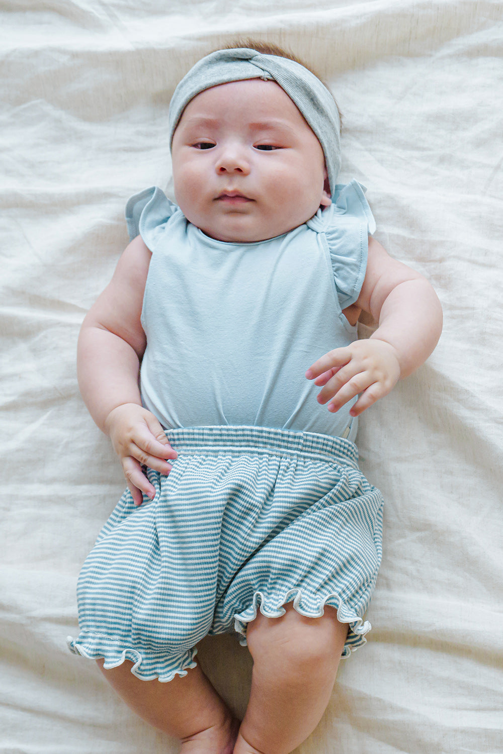 Happy infant in Avauma Mellow Stripe Set Aquamint. Baby smiling and looking at camera in a soft blue striped romper. Happy infant in Avauma Mellow Stripe Set Aquamint. Baby smiling and looking at camera in a soft blue striped romper.