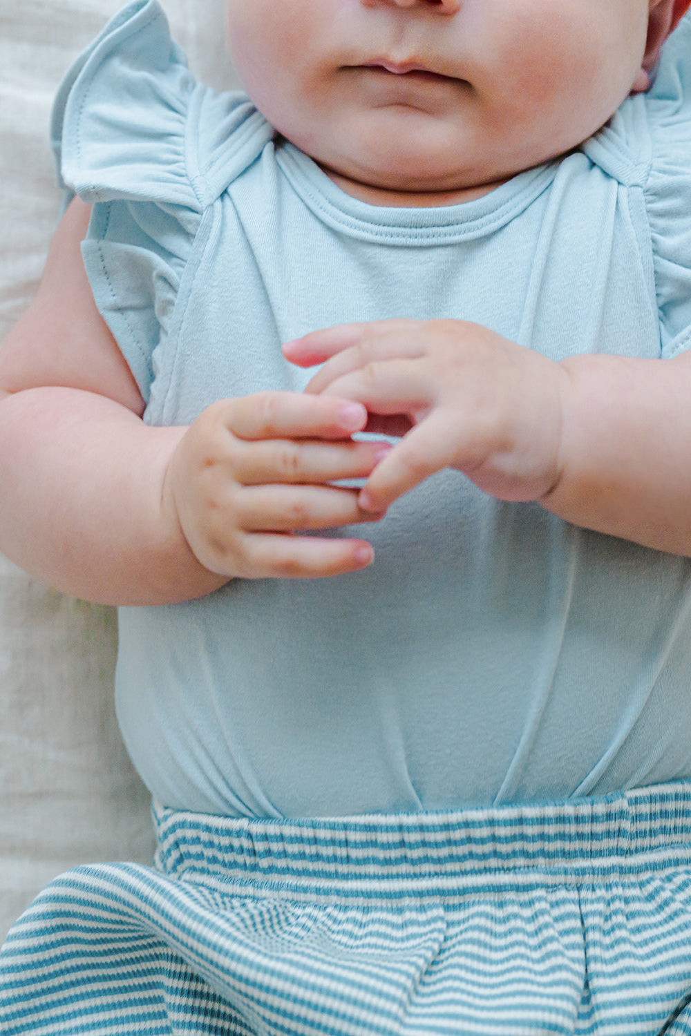 Close-up of baby wearing Avauma Mellow Stripe Set Aquamint. Infant's hands and upper body in a soft blue striped outfit. Close-up of baby wearing Avauma Mellow Stripe Set Aquamint. Infant's hands and upper body in a soft blue striped outfit.