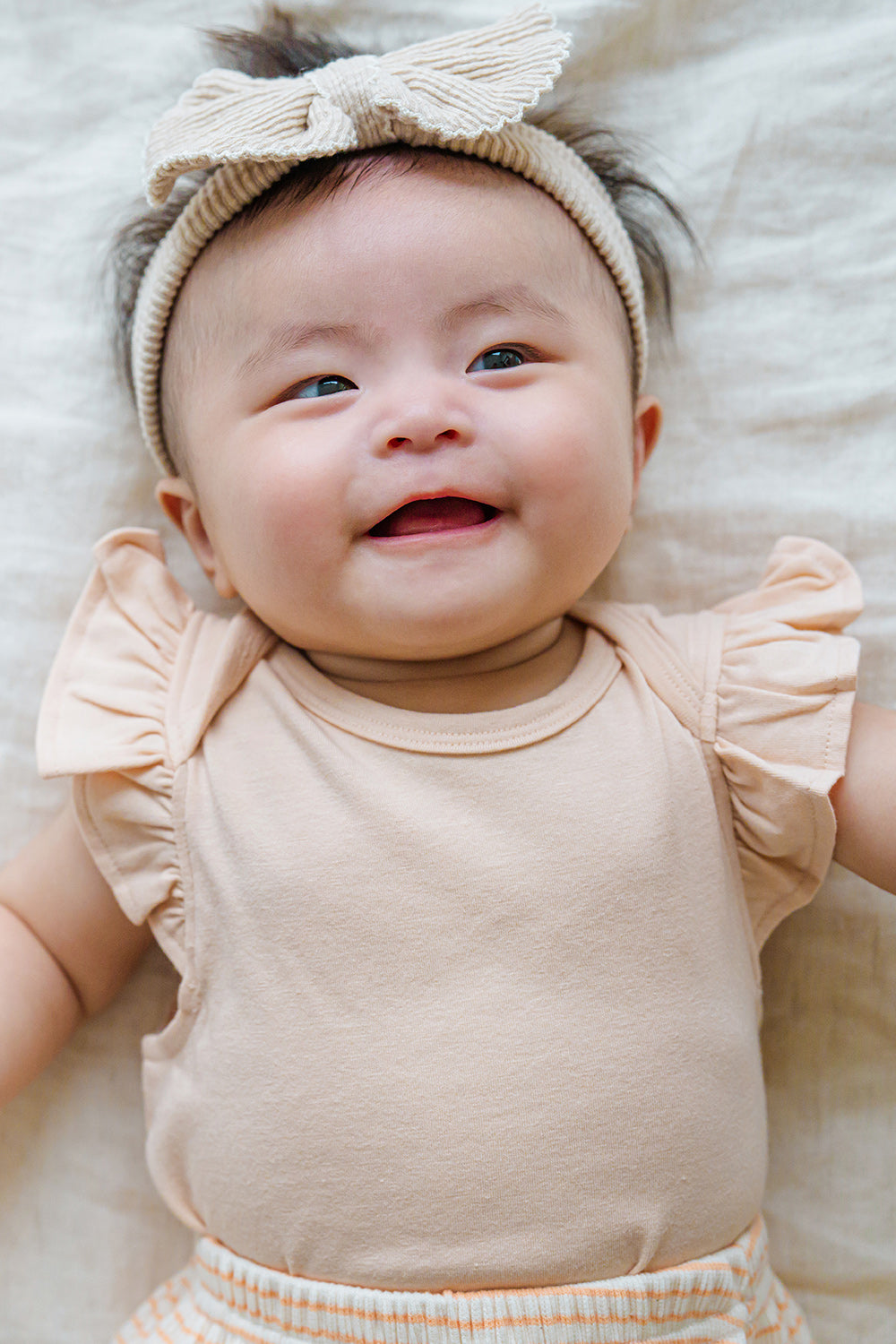 Smiling baby in Avauma Mellow Stripe Set Peach Macaron. Infant looking at camera in a sweet peach striped romper. Smiling baby in Avauma Mellow Stripe Set Peach Macaron. Infant looking at camera in a sweet peach striped romper.