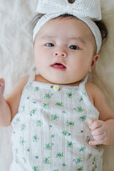 Cute baby face in Avauma Summer Picot Sleeveless Bodysuit Blue Garden Mint. Infant looking at camera, wearing floral romper and white lace bow headband. Cute baby face in Avauma Summer Picot Sleeveless Bodysuit Blue Garden Mint. Infant looking at camera, wearing floral romper and white lace bow headband.