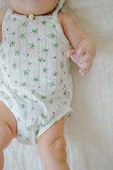 Close-up of Avauma Summer Picot Sleeveless Bodysuit Blue Garden Mint. Detail of white romper with blue and green floral pattern on baby's torso. Close-up of Avauma Summer Picot Sleeveless Bodysuit Blue Garden Mint. Detail of white romper with blue and green floral pattern on baby's torso.