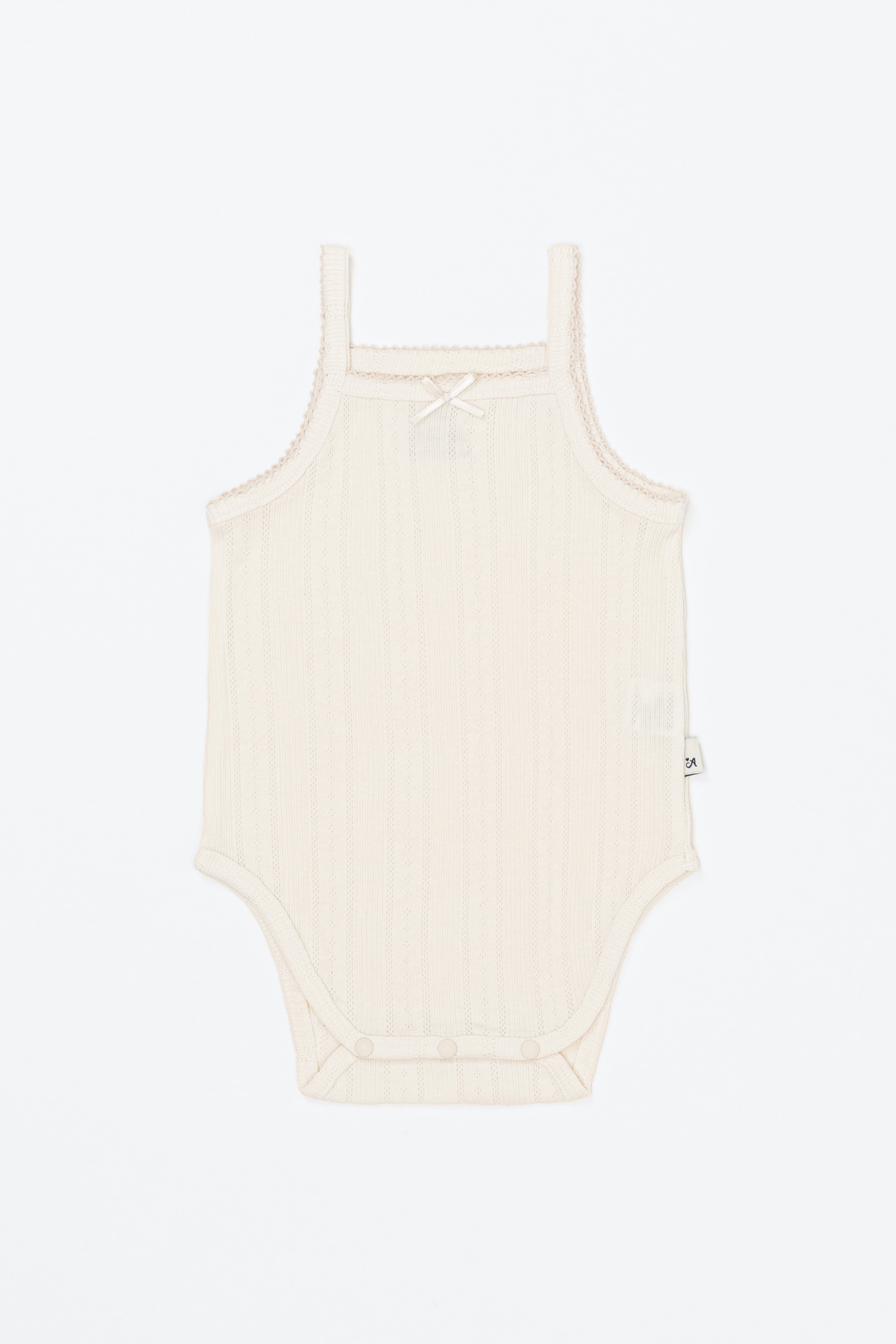 Avauma Summer Picot Sleeveless Bodysuit Buttermilk product shot. Lay-flat of white ribbed baby romper with small bow on a clean background. Avauma Summer Picot Sleeveless Bodysuit Buttermilk product shot. Lay-flat of white ribbed baby romper with small bow on a clean background.