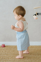 Side profile of toddler in Avauma Sunny Stripe Pants Blueberry Powder. Baby standing in light blue striped shorts and a sleeveless white top.
Side profile of toddler in Avauma Sunny Stripe Pants Blueberry Powder. Baby standing in light blue striped shorts and a sleeveless white top.