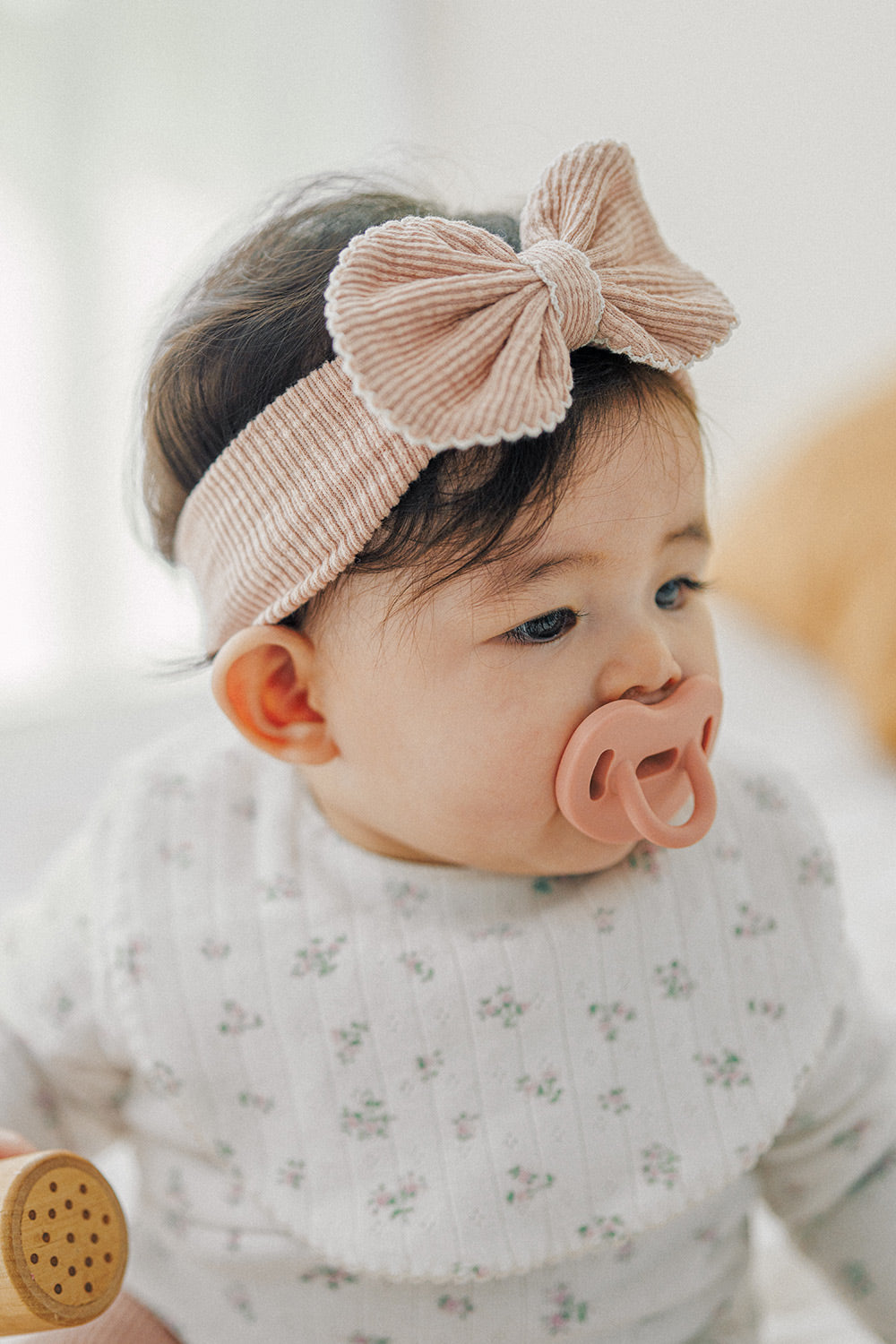 Side view of baby girl wearing Avauma Mellow Ribbon Band in Baby Blush with pacifier
 Side view of baby girl wearing Avauma Mellow Ribbon Band in Baby Blush with pacifier