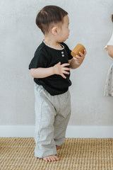 Baby wearing Avauma Breeze Jogger Pants in vintage check, holding bread toy and walking indoors. Baby wearing Avauma Breeze Jogger Pants in vintage check, holding bread toy and walking indoors.