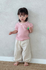 Child standing in Avauma Breeze Jogger Pants - roseberry cream, holding flower, playful pose. Child standing in Avauma Breeze Jogger Pants - roseberry cream, holding flower, playful pose.