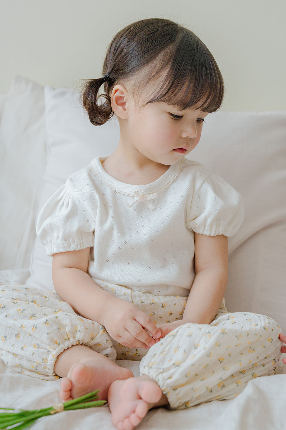 Child sitting on bed in Avauma Breeze Jogger Pants with yellow floral pattern, paired with white puff-sleeve top. Child sitting on bed in Avauma Breeze Jogger Pants with yellow floral pattern, paired with white puff-sleeve top.