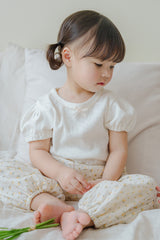 Child sitting on bed in Avauma Breeze Jogger Pants with yellow floral pattern, paired with white puff-sleeve top. Child sitting on bed in Avauma Breeze Jogger Pants with yellow floral pattern, paired with white puff-sleeve top.