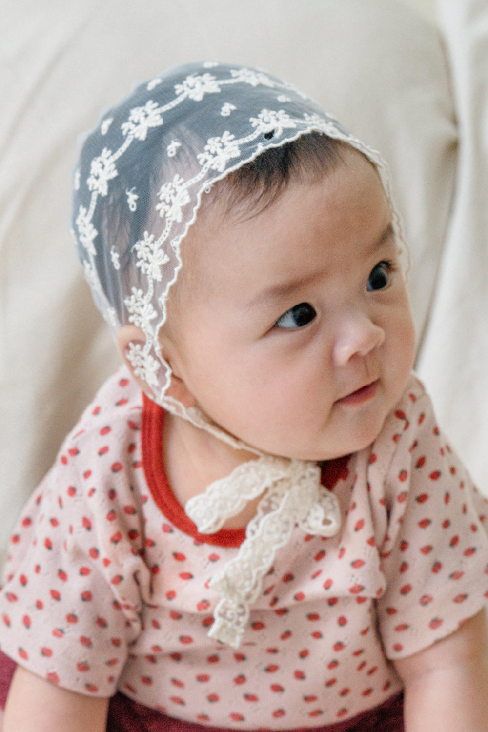baby girl wearing avauma Clare Bonnet Ivory Race, sitting and looking to the side in dotted outfit baby girl wearing avauma Clare Bonnet Ivory Race, sitting and looking to the side in dotted outfit