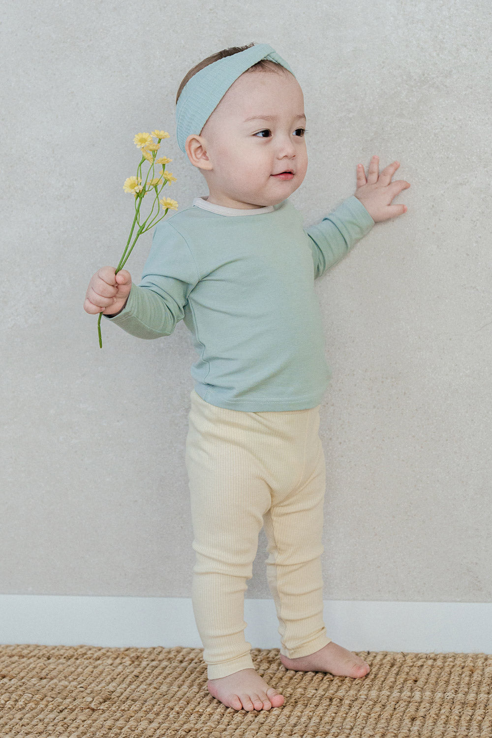 Baby wearing the Sage Leaf top and ribbed leggings, standing against a wall – showcasing a clean round-neck design and contrasting trim detail Baby wearing the Sage Leaf top and ribbed leggings, standing against a wall – showcasing a clean round-neck design and contrasting trim detail