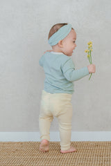 Back view of a smiling baby holding yellow flowers – highlighting the comfortable waistband of the Avauma Cloud Ribbed Setup in Sage Leaf for unrestricted movement Back view of a smiling baby holding yellow flowers – highlighting the comfortable waistband of the Avauma Cloud Ribbed Setup in Sage Leaf for unrestricted movement
