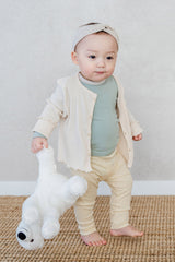 Baby standing with a stuffed toy – wearing a cream-colored cardigan over the Avauma Cloud Ribbed Setup in Sage Leaf for a warm, cozy look Baby standing with a stuffed toy – wearing a cream-colored cardigan over the Avauma Cloud Ribbed Setup in Sage Leaf for a warm, cozy look