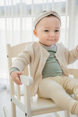 Baby sitting in a chair – highlighting the button detail on the Avauma Cloud Ribbed Setup top in Sage Leaf and the ribbed leggings for a comfy yet stylish vibe Baby sitting in a chair – highlighting the button detail on the Avauma Cloud Ribbed Setup top in Sage Leaf and the ribbed leggings for a comfy yet stylish vibe