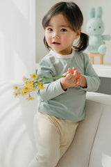 Child posing with yellow flowers in the Sage Leaf top – featuring a cozy pastel hue and relaxed silhouette suitable for everyday wear or outings Child posing with yellow flowers in the Sage Leaf top – featuring a cozy pastel hue and relaxed silhouette suitable for everyday wear or outings