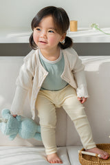 Child wearing the Avauma Cloud Ribbed Setup in Sage Leaf, standing on a sofa with flowers – featuring a soft fabric and stretchy ribbed material for a comfortable, natural fit Child wearing the Avauma Cloud Ribbed Setup in Sage Leaf, standing on a sofa with flowers – featuring a soft fabric and stretchy ribbed material for a comfortable, natural fit