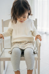 Baby girl sitting on chair wearing Avauma mint green baby skirt leggings and ribbed ivory top Baby girl sitting on chair wearing Avauma mint green baby skirt leggings and ribbed ivory top