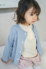 Infant girl wearing Avauma blue baby cardigan layered over heart-pattern onesie, soft cotton babywear Infant girl wearing Avauma blue baby cardigan layered over heart-pattern onesie, soft cotton babywear