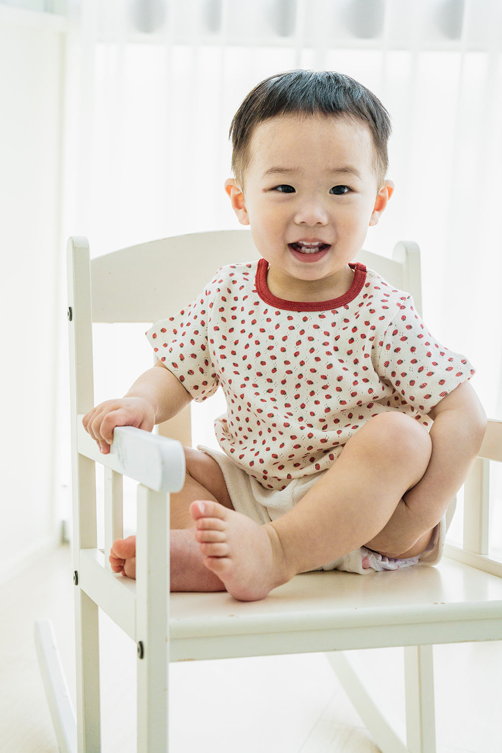 Smiling toddler boy wearing Avauma Ivory Berry Set, sitting on white rocking chair Smiling toddler boy wearing Avauma Ivory Berry Set, sitting on white rocking chair