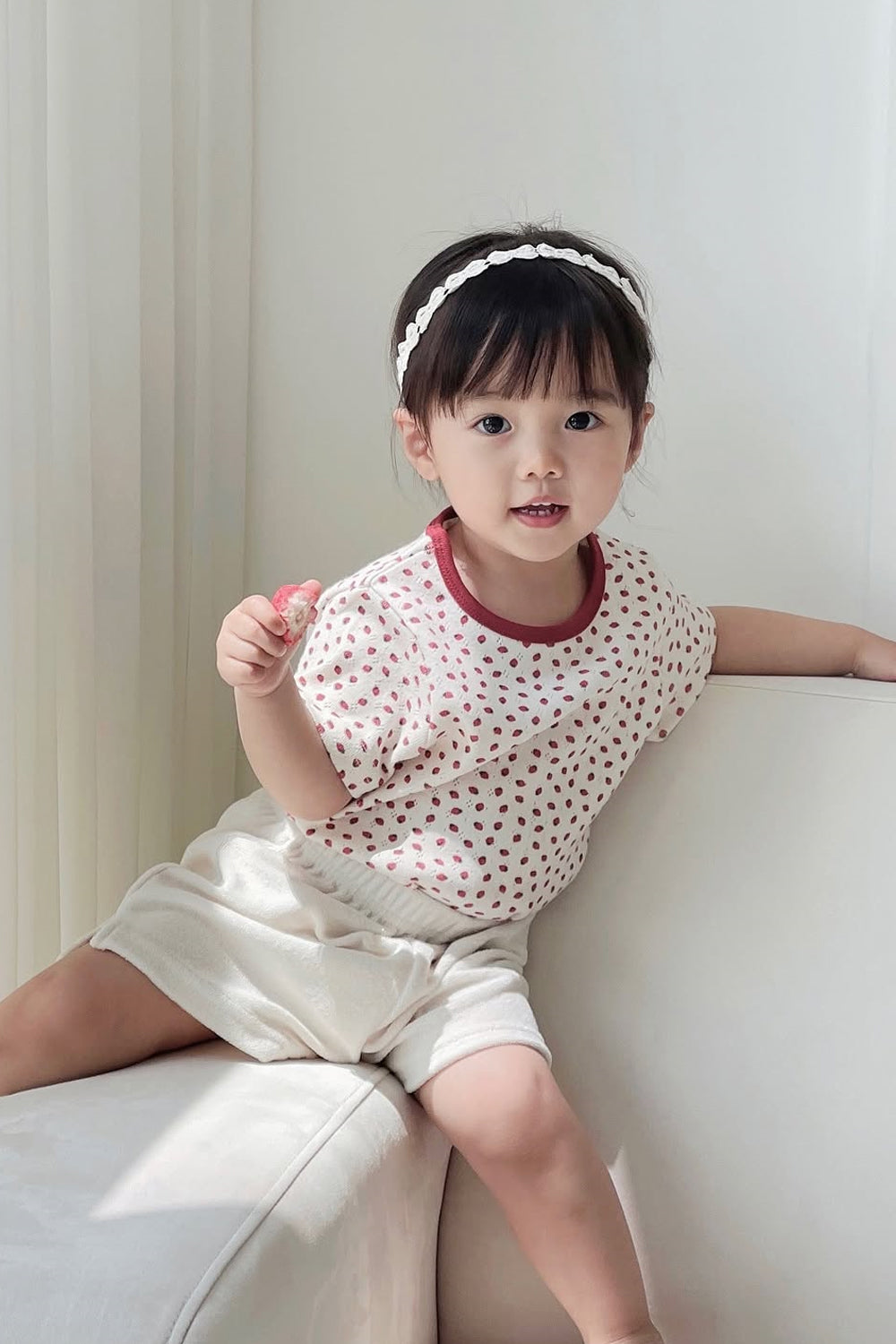 Happy toddler girl smiling in Avauma Ivory Berry outfit, playful pose on couch Happy toddler girl smiling in Avauma Ivory Berry outfit, playful pose on couch