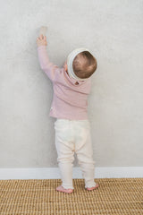 Back view of a baby standing against the wall – highlighting the back button detail and ruffle accents on the ribbed leggings in the Avauma Peach Glow Set in Pale Peach Back view of a baby standing against the wall – highlighting the back button detail and ruffle accents on the ribbed leggings in the Avauma Peach Glow Set in Pale Peach