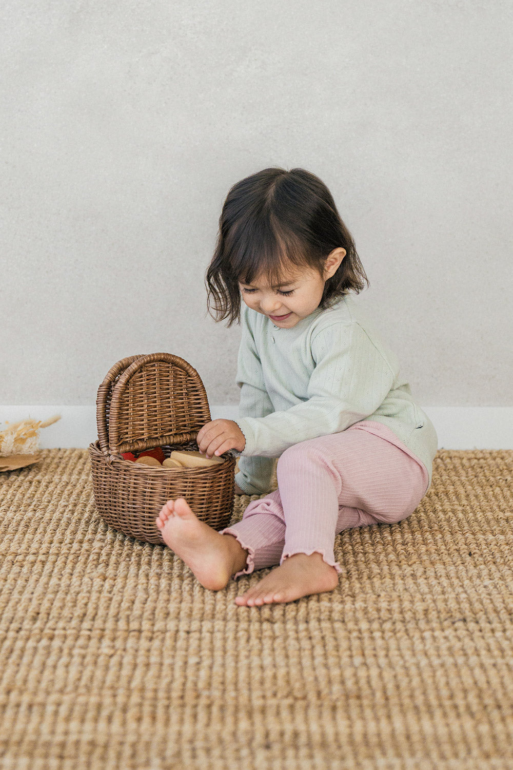 A child playing with a basket while wearing the Avauma Peach Glow Set in Soft Sage – featuring stretchy ribbed leggings and a button-detail top for both coziness and practicality A child playing with a basket while wearing the Avauma Peach Glow Set in Soft Sage – featuring stretchy ribbed leggings and a button-detail top for both coziness and practicality