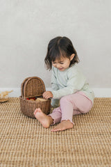 A child playing with a basket while wearing the Avauma Peach Glow Set in Soft Sage – featuring stretchy ribbed leggings and a button-detail top for both coziness and practicality A child playing with a basket while wearing the Avauma Peach Glow Set in Soft Sage – featuring stretchy ribbed leggings and a button-detail top for both coziness and practicality
