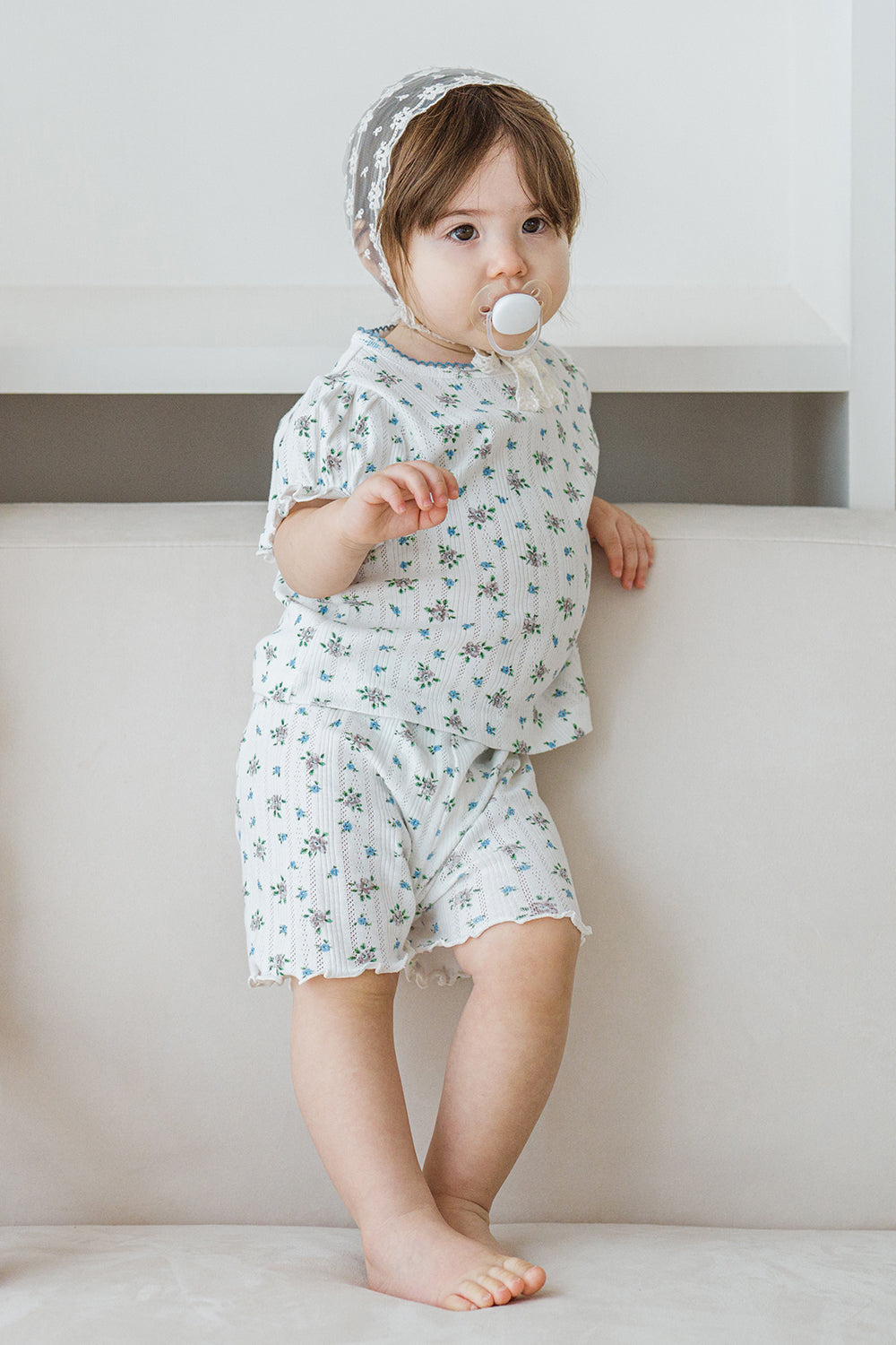 Toddler in Avauma Petit Ruffle Bluebell short sleeve outfit, standing on a white sofa.
Toddler in Avauma Petit Ruffle Bluebell short sleeve outfit, standing on a white sofa.