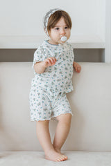 Toddler in Avauma Petit Ruffle Bluebell short sleeve outfit, standing on a white sofa.
Toddler in Avauma Petit Ruffle Bluebell short sleeve outfit, standing on a white sofa.