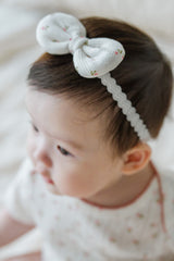 Close-up of baby wearing Avauma Rose Garden Petite Garden Headband with delicate pink rose floral bow Close-up of baby wearing Avauma Rose Garden Petite Garden Headband with delicate pink rose floral bow