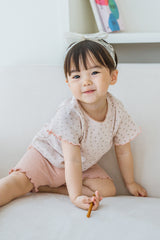 Toddler girl smiling in Pure Hug rosy blush summer set, sitting on a sofa, wearing pink shorts and floral top.
Toddler girl smiling in Pure Hug rosy blush summer set, sitting on a sofa, wearing pink shorts and floral top.