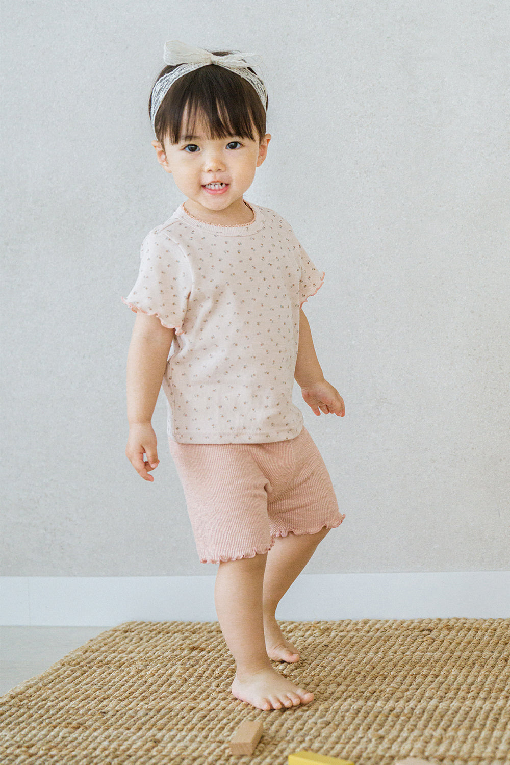 Toddler girl standing on rug in rosy blush Pure Hug baby summer set, pink ribbed shorts and floral top, playful expression.
Toddler girl standing on rug in rosy blush Pure Hug baby summer set, pink ribbed shorts and floral top, playful expression.