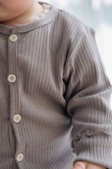 Close-up of Avauma baby ribbed cardigan in Ash Beige, soft cotton texture with delicate frill sleeve Close-up of Avauma baby ribbed cardigan in Ash Beige, soft cotton texture with delicate frill sleeve