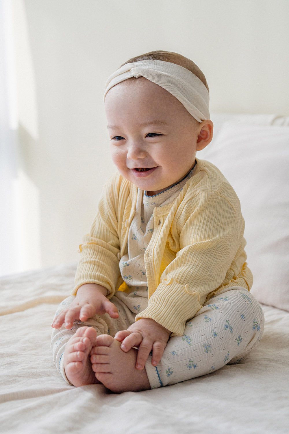 Baby girl wearing Avauma butter yellow cardigan over floral romper, cute infant outfit idea with headband Baby girl wearing Avauma butter yellow cardigan over floral romper, cute infant outfit idea with headband