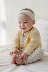 Baby girl wearing Avauma butter yellow cardigan over floral romper, cute infant outfit idea with headband Baby girl wearing Avauma butter yellow cardigan over floral romper, cute infant outfit idea with headband