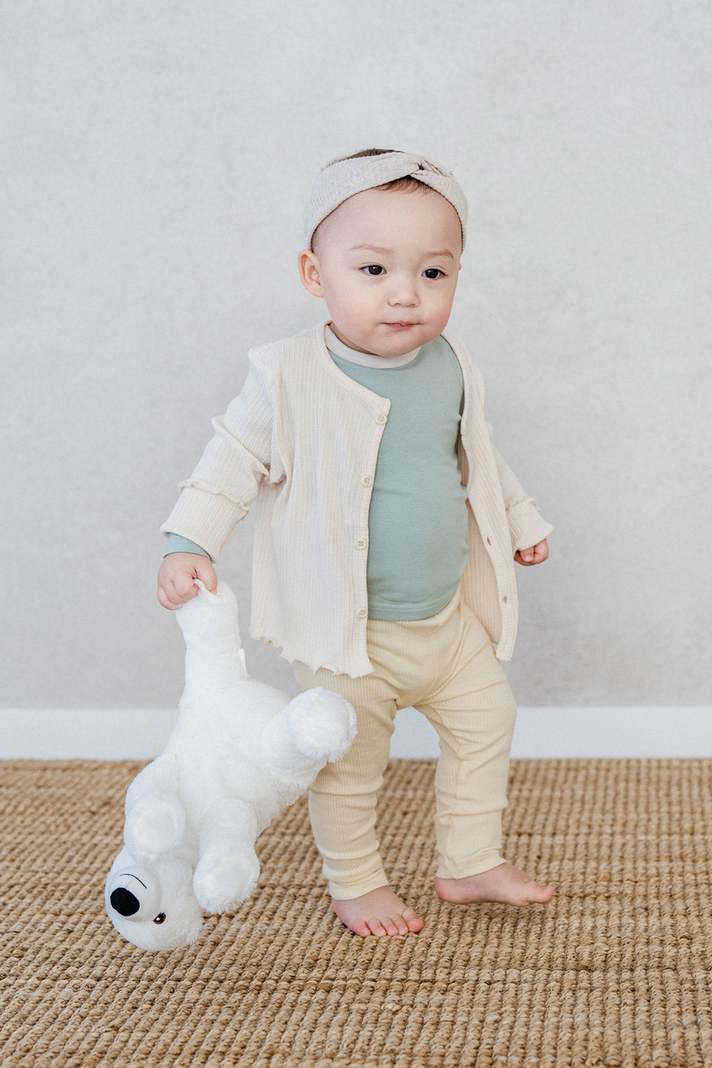 Toddler standing on a rug in Avauma off white cardigan set, holding a white teddy bear Toddler standing on a rug in Avauma off white cardigan set, holding a white teddy bear